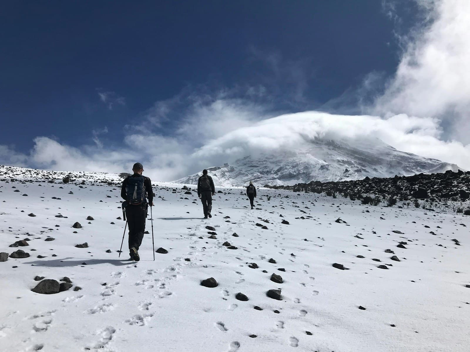 Tres montañistas suben por la nieve hacia el Chimborazo, con la cumbre entre nubes.